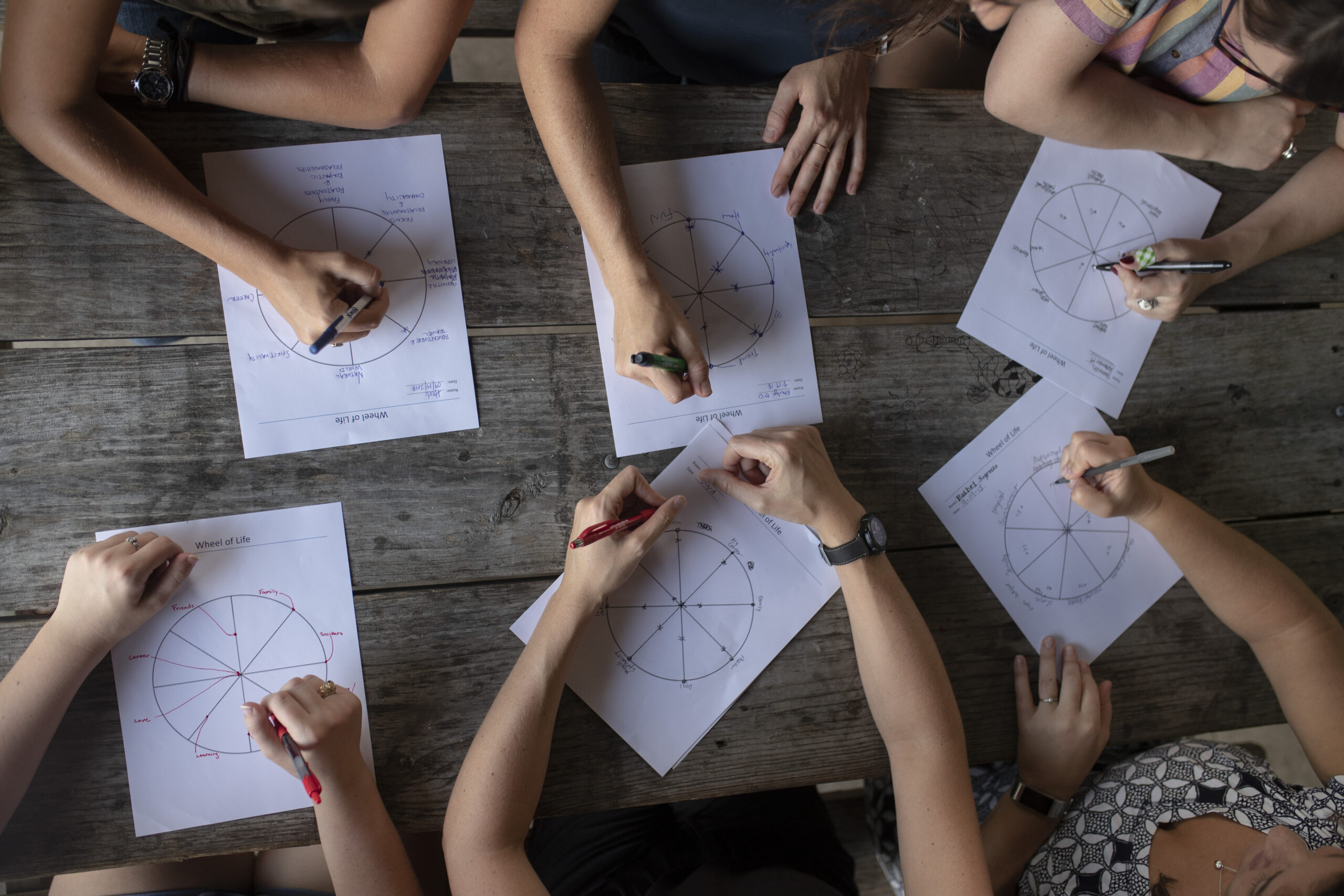 top down view of several sets of hands writing on paper on a table