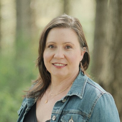 White woman in a jean jacket with trees in the background