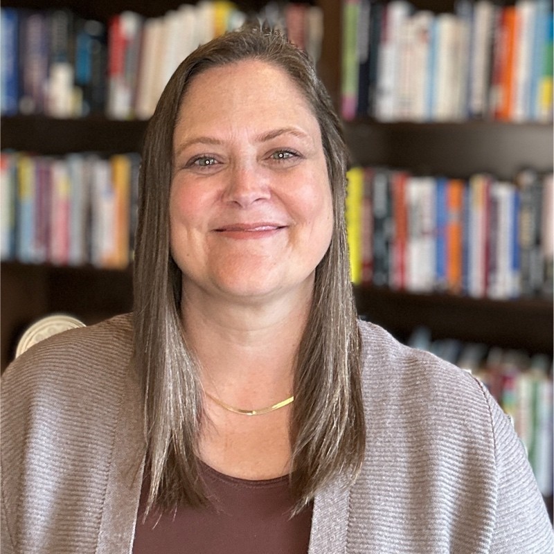 White woman with long straight hair smiling in front of a book shelf